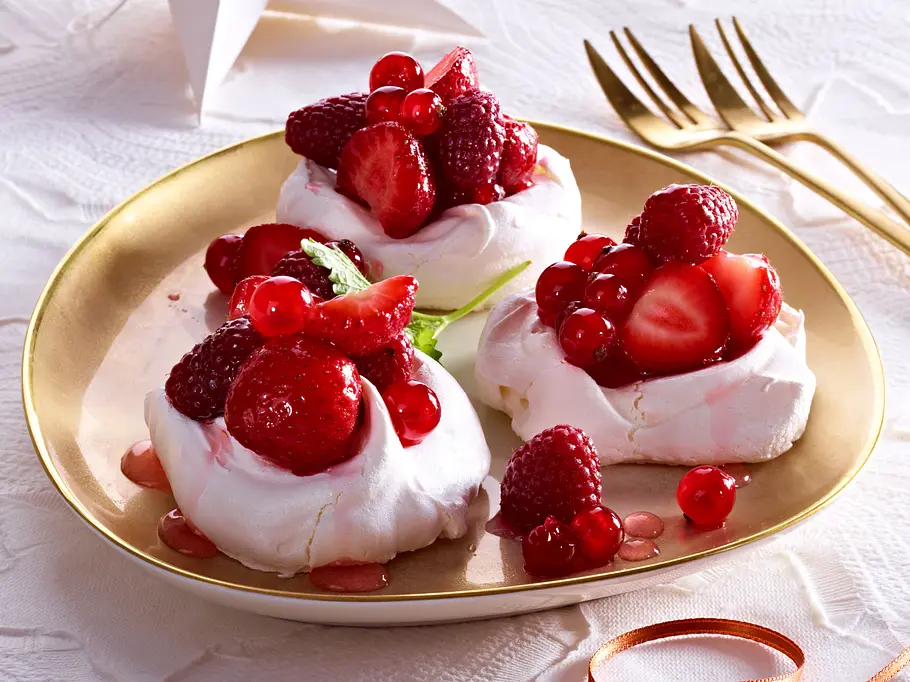 3 Mini-Pavlovas mit roten Früchten auf einem goldenen Teller.