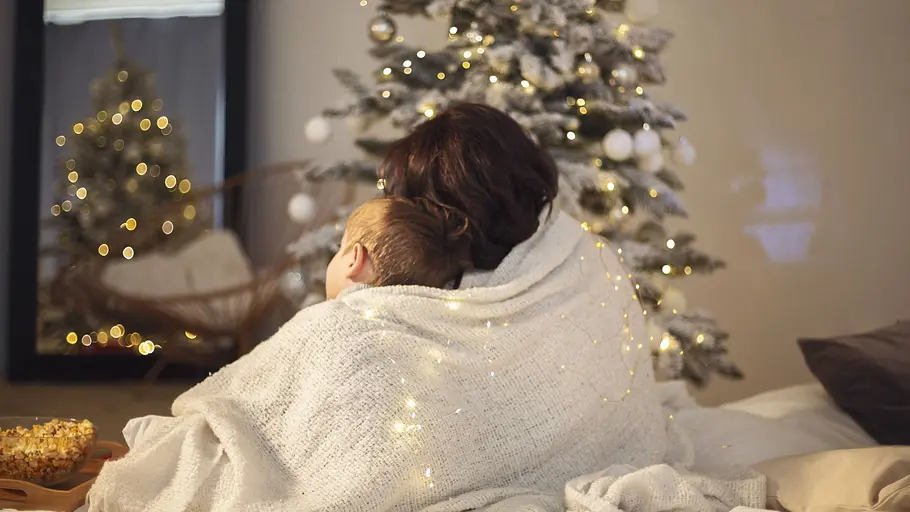 Weihnachtsfilm Mutter und Kind kuscheln Eine Frau sitzt eingekuschelt in einer Decke mit ihrem Kind vor dem Fernseher. Es ist weihnachtlich dekoriert.