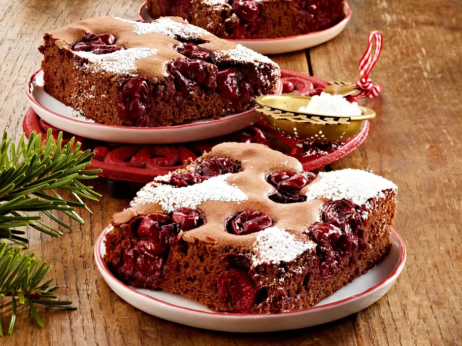 Weihnachtskuchen: Glühwein-Kuchen vom Blech Stücke vom weihnachtlichen Blechkuchen mit Schokolade und Kirschen liegen auf Tellern.