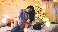 Junges, verliebtes, heterosexuelles Paar auf einem Bett neben ihnen ein Weihnachtsbaum. Sie trägt einen lila Pullover und sitzt auf ihm. Er hält ihre Hände und ist unter ihr ausgestreckt. - Foto: Vasyl Dolmatov/iStock Junges, verliebtes, heterosexuelles Paar auf einem Bett neben ihnen ein Weihnachtsbaum. Sie trägt einen lila Pullover und sitzt auf ihm. Er hält ihre Hände und ist unter ihr ausgestreckt. - Foto: Vasyl Dolmatov/iStock