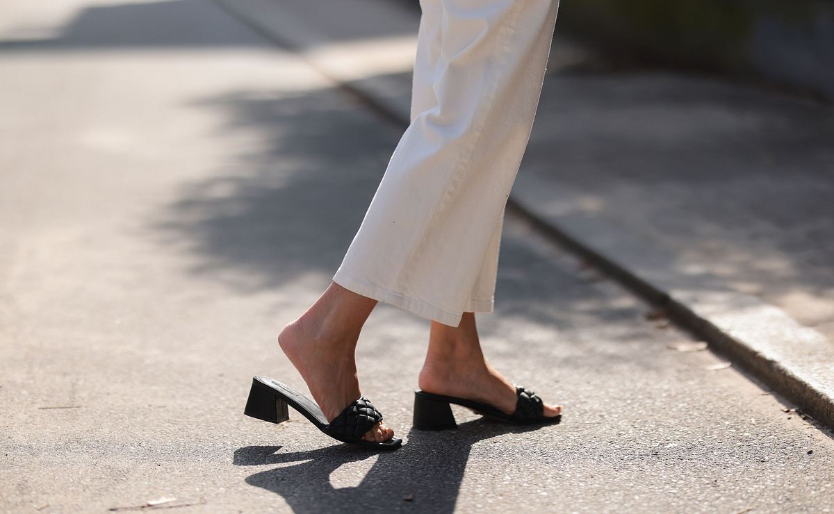 Weiße, weite über dem Knöchel abgeschnittene, weiße Jeans kombiniert mit schwarzen offenen Pantoletten mit kleinem Absatz.