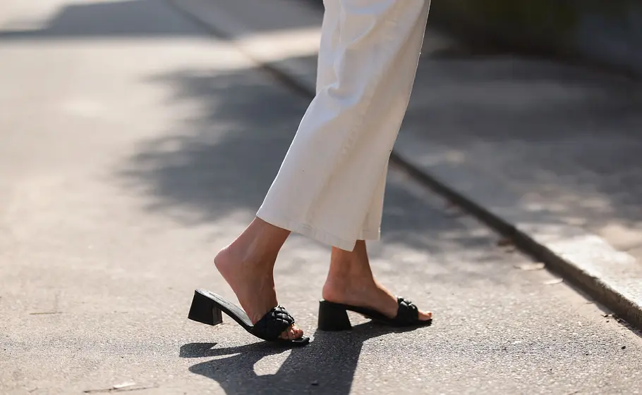 Welche Schuhe zur weißen Jeans? Weiße, weite über dem Knöchel abgeschnittene, weiße Jeans kombiniert mit schwarzen offenen Pantoletten mit kleinem Absatz.