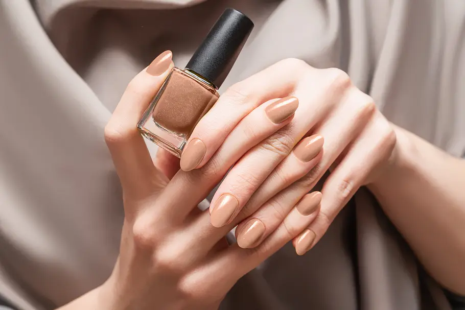 Welcher Nagellack hält am längsten Beige lackierte Frauenhände halten einen Nagellack