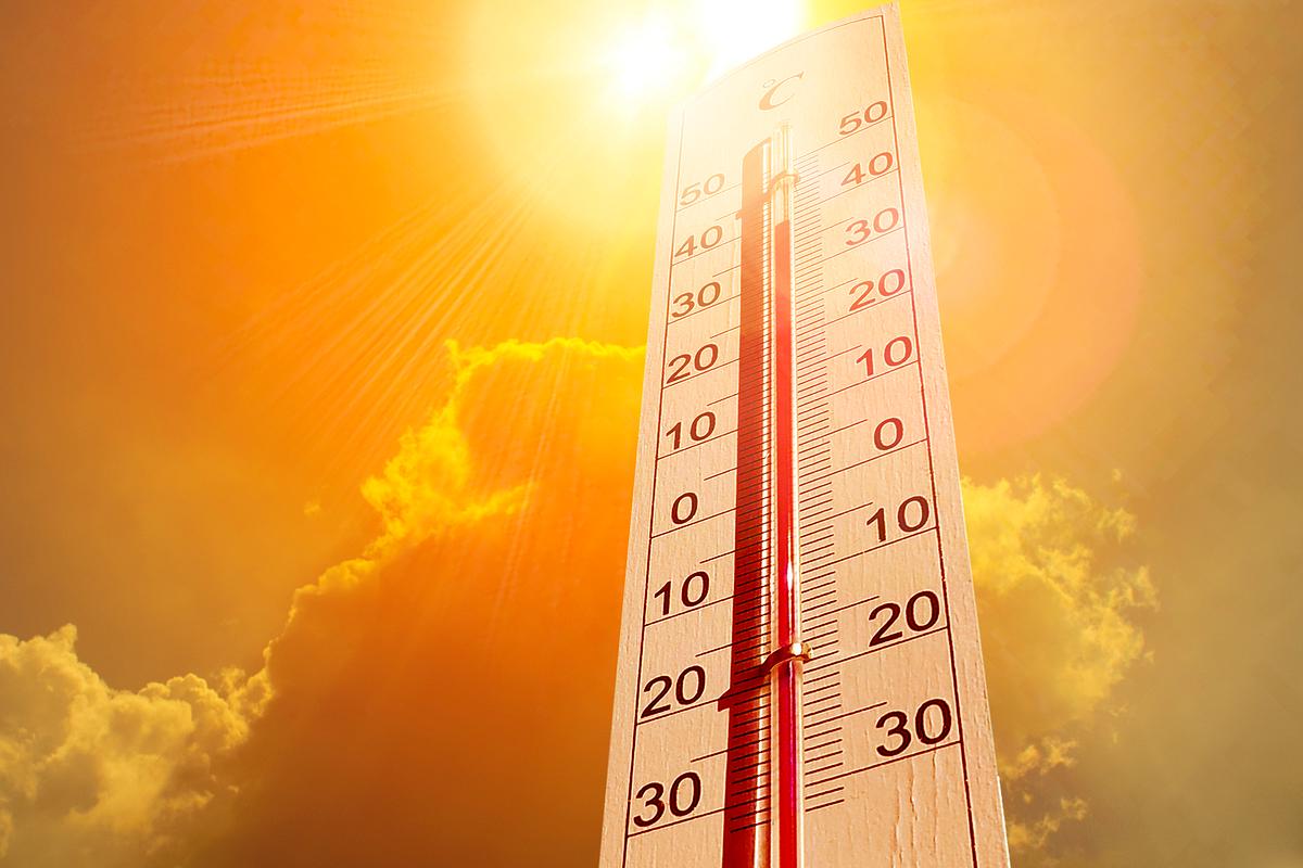 Thermometer vor praller Sonne und einer Wolke weist auf sommerliche Temperaturen hin.