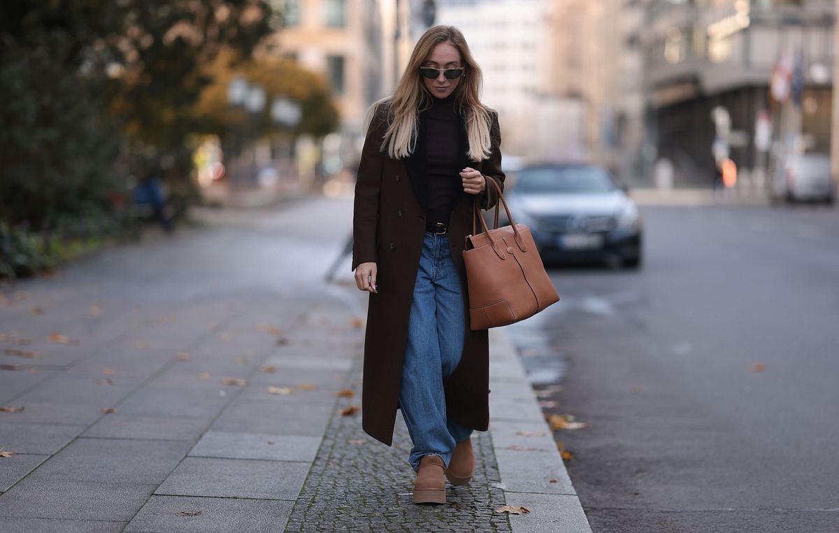 Frau läuft die Straße entlang und trägt passend zur weiten Jeans einen langen Mantel. 