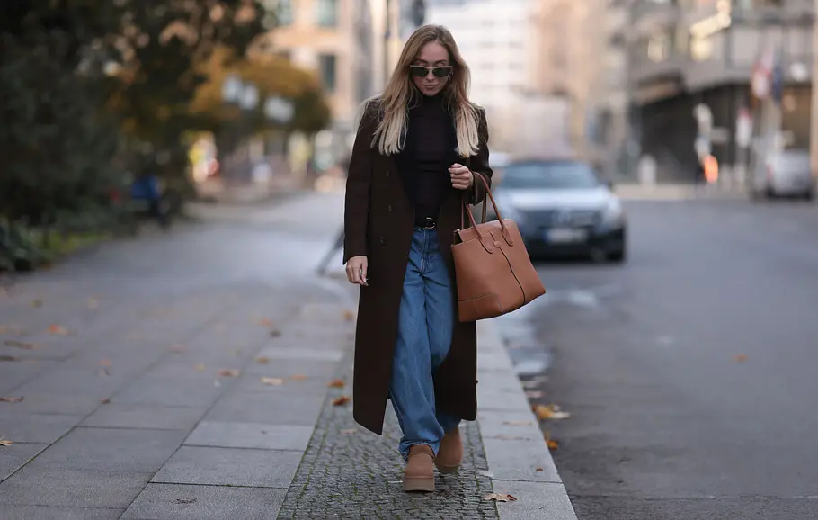 Frau läuft die Straße entlang und trägt passend zur weiten Jeans einen langen Mantel. 
