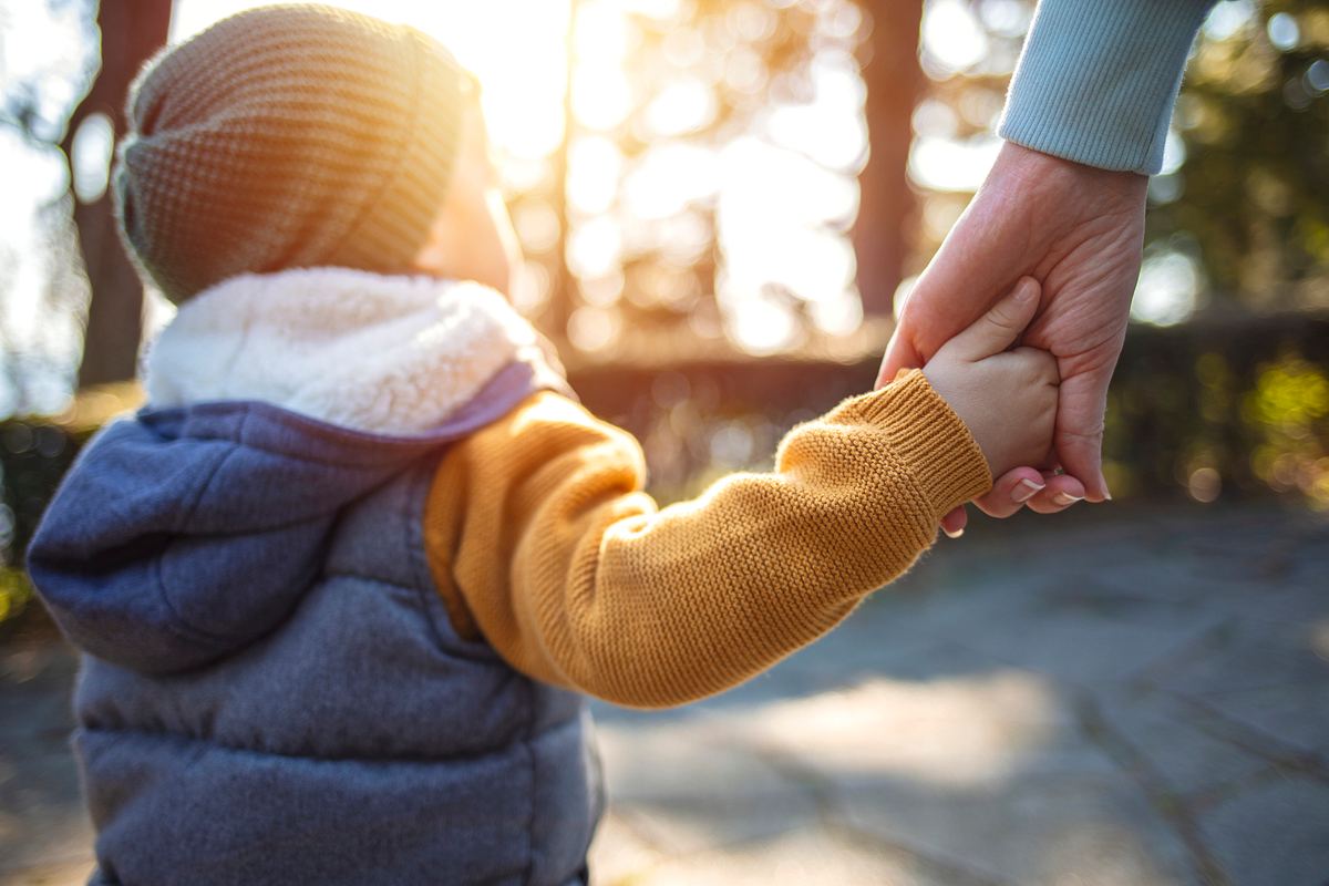 Zu sehen ist ein Kind von hinten, das die Hand eines erwachsenen hält.
