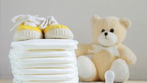 Ein Stapel Windeln neben einem Plüschteddy, gelben Babyschuhen und einem Babyschnuller - Foto: iStock/JuanCi