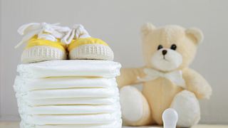 Ein Stapel Windeln neben einem Plüschteddy, gelben Babyschuhen und einem Babyschnuller - Foto: iStock/JuanCi