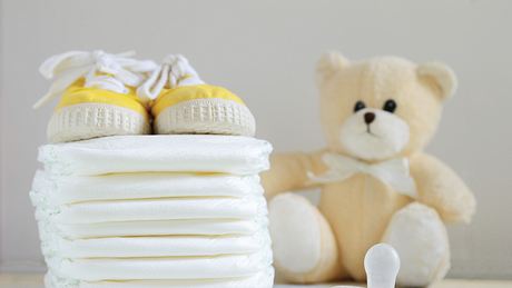 Ein Stapel Windeln neben einem Plüschteddy, gelben Babyschuhen und einem Babyschnuller - Foto: iStock/JuanCi