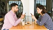 Paar sitzt sich gegenüber am Tisch, beide schauen in ihr Smartphone (Themenbild) - Foto: Antonio_Diaz / iStock