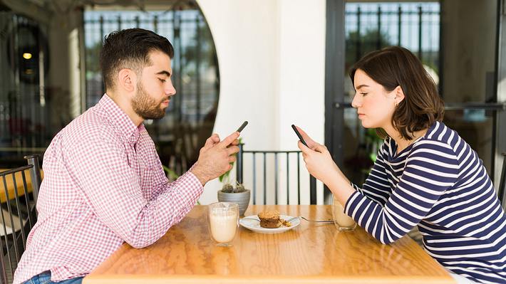 Paar sitzt sich gegenüber am Tisch, beide schauen in ihr Smartphone (Themenbild) - Foto: Antonio_Diaz / iStock