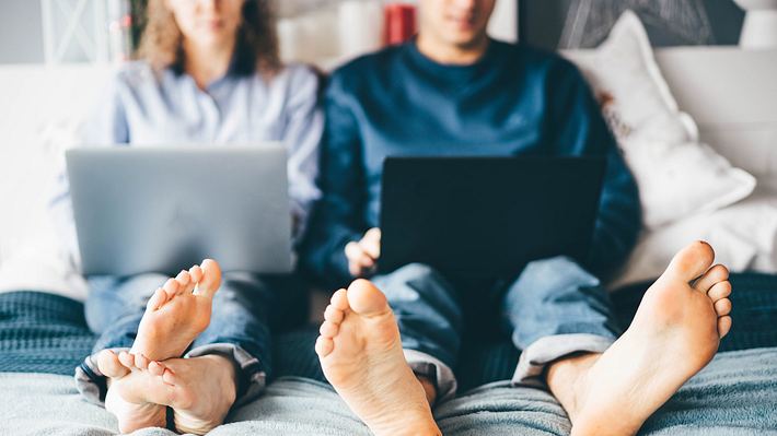 Boyfriend and girlfriend using laptop and working while sitting on bed. - Foto: Maria Korneeva/iStock