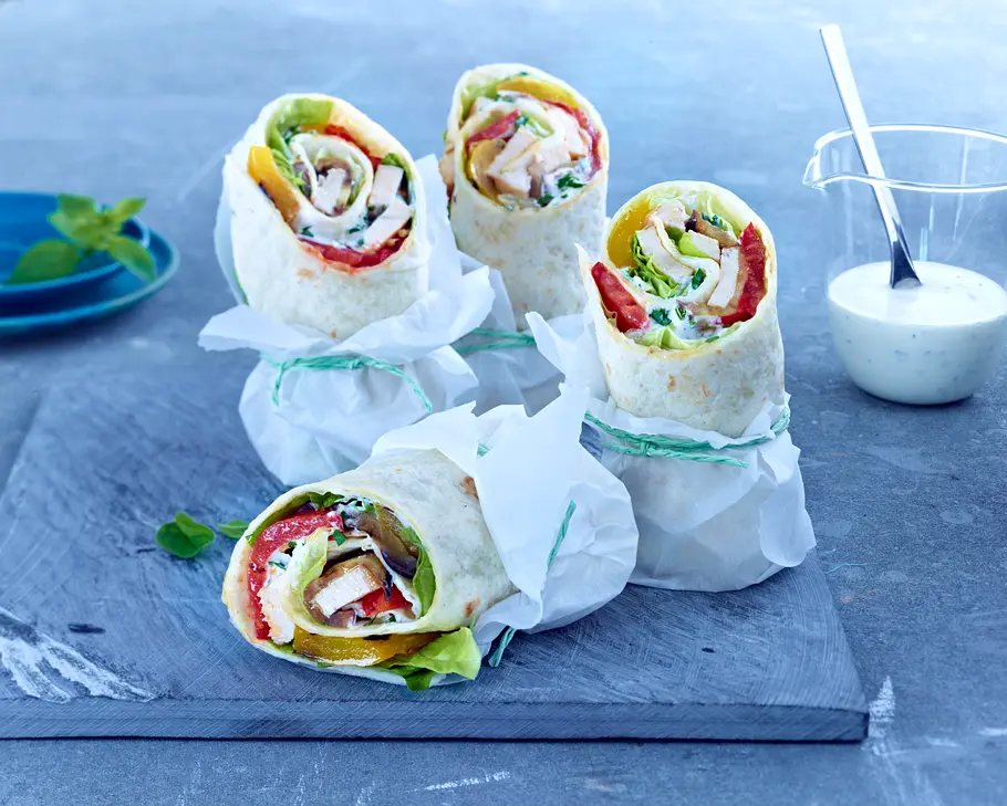 Wrap mit Gemüse: Ein Rezept mit viel Eiweiß 4 kleine Wraps in weißem Backpapier eingewickelt und mit Salat und Hähnchen gefüllt.